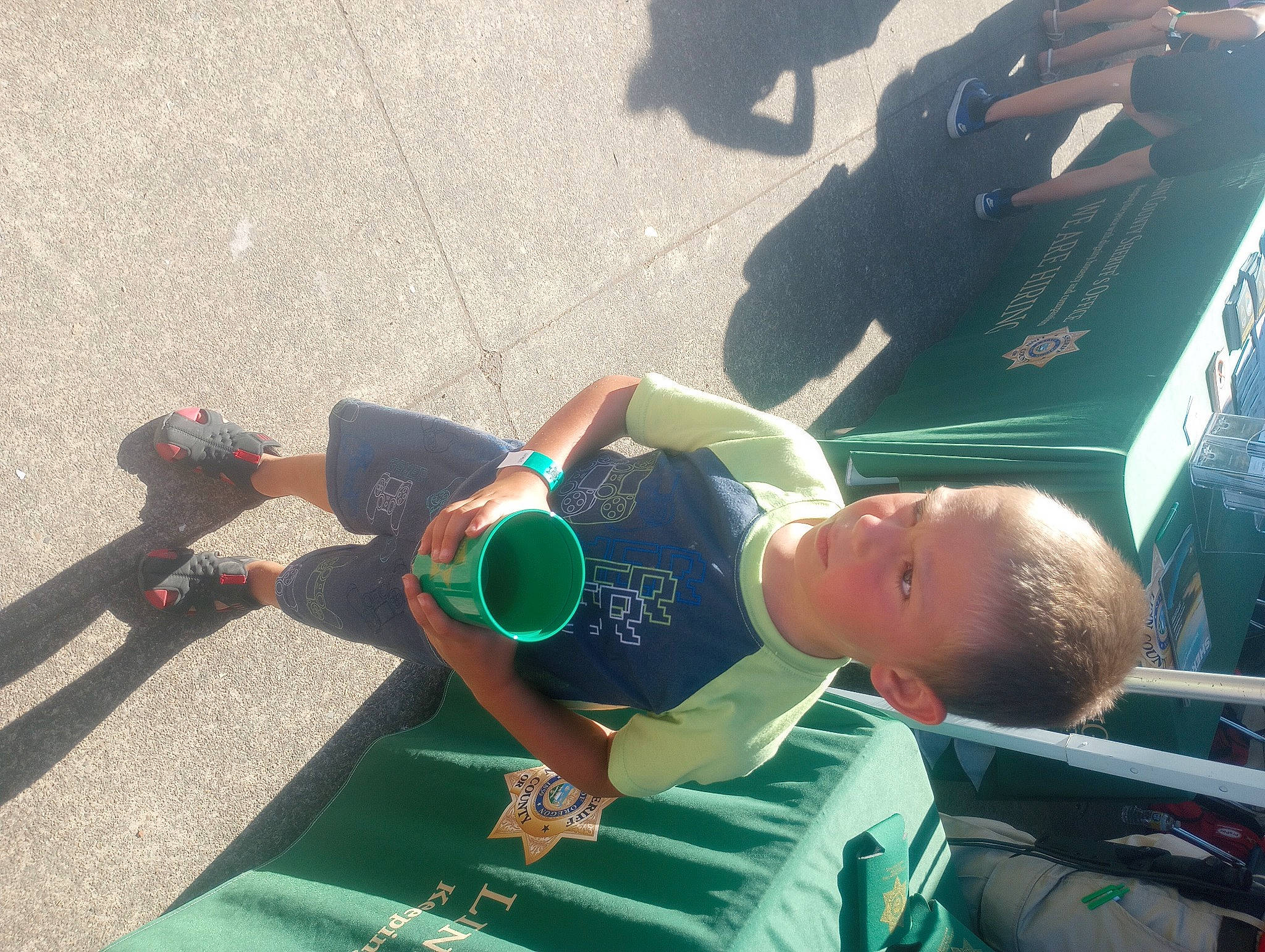 Drake is registered to the contest to win money with this photo: asphalt, baseball_cap, child, elbow, fun, grass, green, hat, human_leg, knee, leisure, pedestrian, person, recreation, shorts, sitting, snapshot, t_shirt, thigh, toddler