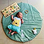 baby, sleeping, milestone_blanket, green, giraffe, toy, wooden_puzzle, name_puzzle, numbers, floor_tiles, infant, cute, child, peaceful, clothing, soft_toy, playful, portrait, lying_down, indoors