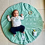 baby, baby_boy, baby_girl, calm, child, clothing, cute, floor, giraffe, green_mat, indoor, infant, lying_down, mat, numbers, pants, portrait, shirt, tile_floor, toy