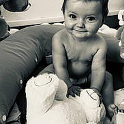 Malia a rejoint le concours — aidez-le/la à gagner de superbes lots ! baby, child, smile, face, hair_bow, plush_toy, stuffed_animal, bear, play_area, cushion, sitting, indoors, cute, infant, portrait, happy, monochrome, black_and_white, toy, person