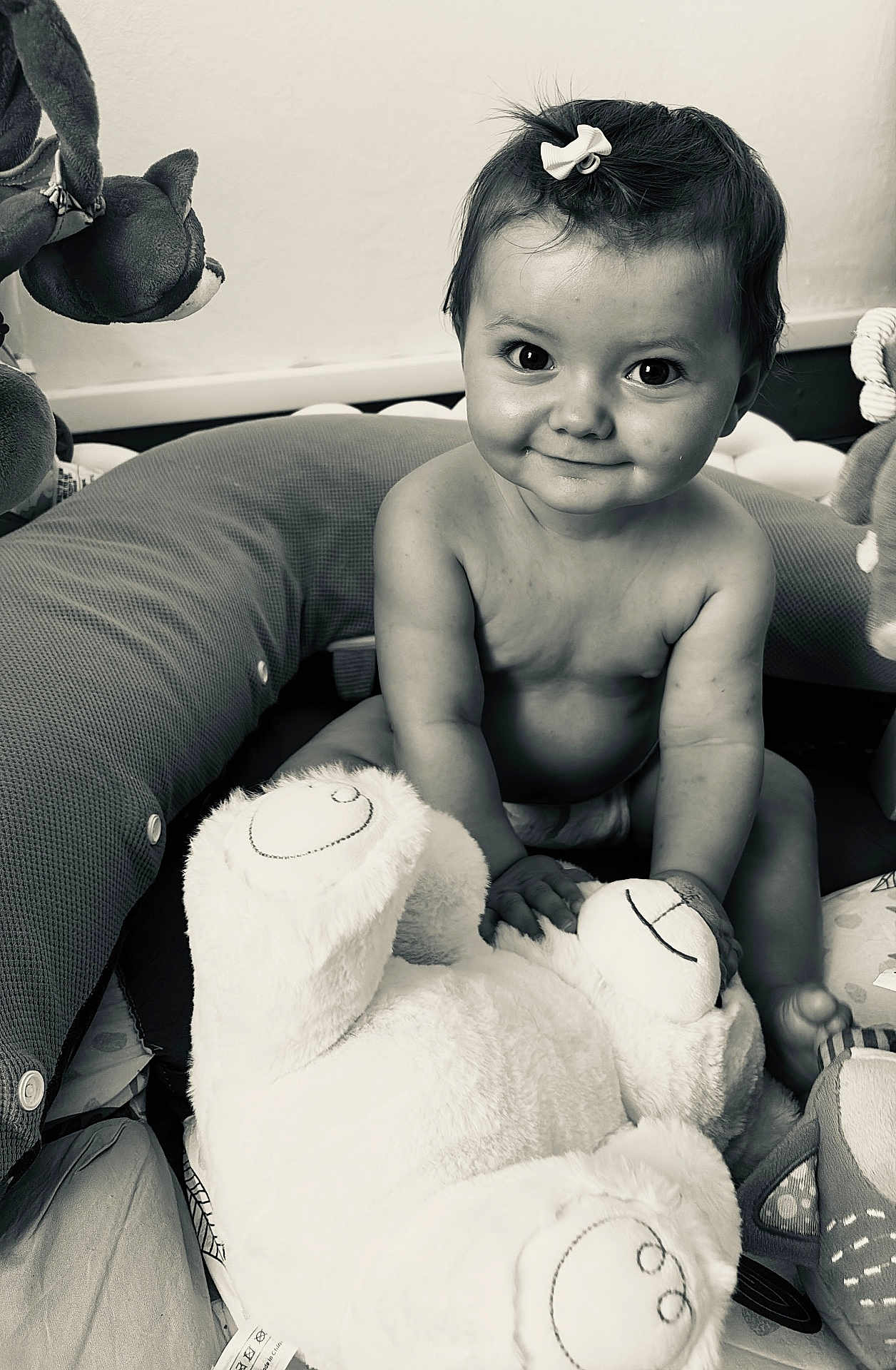 Malia a rejoint le concours — aidez-le/la à gagner de superbes lots ! baby, child, smile, face, hair_bow, plush_toy, stuffed_animal, bear, play_area, cushion, sitting, indoors, cute, infant, portrait, happy, monochrome, black_and_white, toy, person