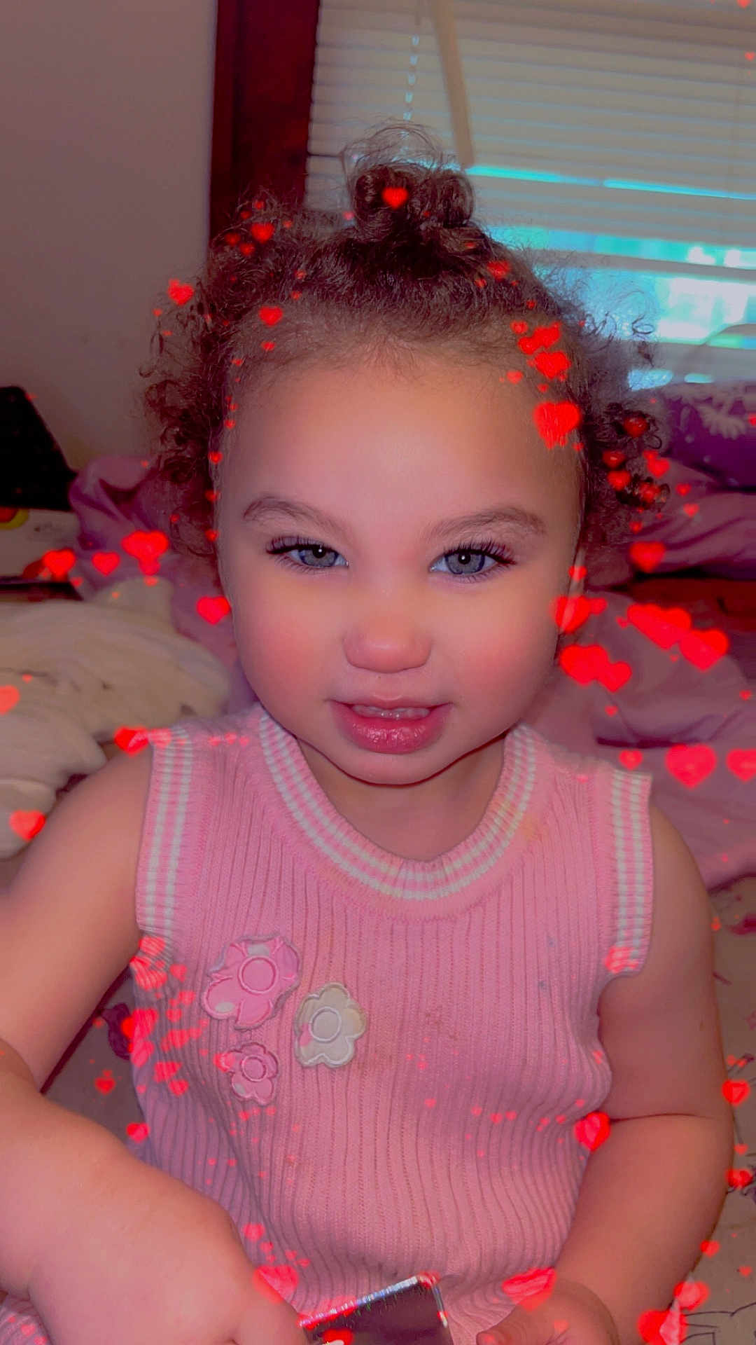 Saylor joined the competition — help win amazing prizes! toddler, child, girl, curly_hair, pink_sweater, flower_patch, indoor, window, bed, bedding, holding_object, heart_effect, portrait, cute, smiling, baby, skin, face, person, hairstyle