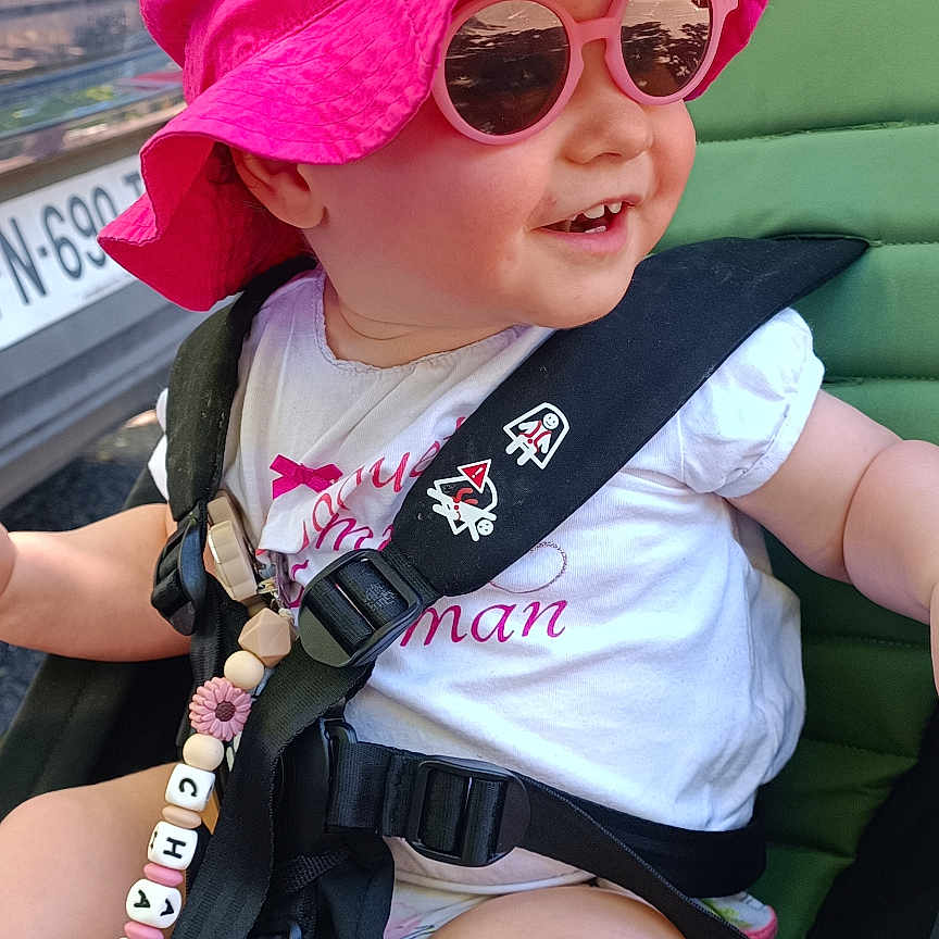 Charlie participe au concours pour gagner de l'argent avec cette photo : arm, baby, beads, bracelet, child, clothing, green, happy, leg, outdoor, pink_hat, reflection, seatbelt, smile, stroller, sunglasses, sunlight, toddler, toy, vehicle
