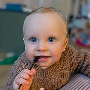 Azel a rejoint le concours — aidez-le/la à gagner de superbes lots ! baby, child, blue_eyes, pen, brown_sweater, hand, face, chewing, indoor, curious, portrait, close_up, person, skin, infant, cute, expression, young_child, fingernails, focus