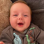 Vinnie is registered to the contest to win money with this photo: baby, smiling, face, infant, clothing, sweatshirt, dinosaur, blanket, cozy, cute, child, person, happy, head, skin, closeup, indoors, young, apparel, portrait