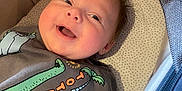 Vinnie joined the competition — help win amazing prizes! baby, smiling, infant, face, clothing, dinosaur, shirt, bassinet, blanket, happy, cute, child, young, indoors, portrait, cozy, lying_down, expression, head, soft_light