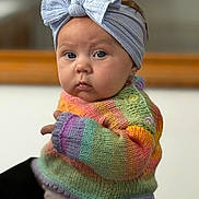 Phoebe is registered to the contest to win money with this photo: baby, child, headband, bow, knitted_sweater, rainbow_colors, cute, portrait, indoor, soft_light, face, chubby_cheeks, expression, person, clothing, infant, warm, colorful, sitting, closeup