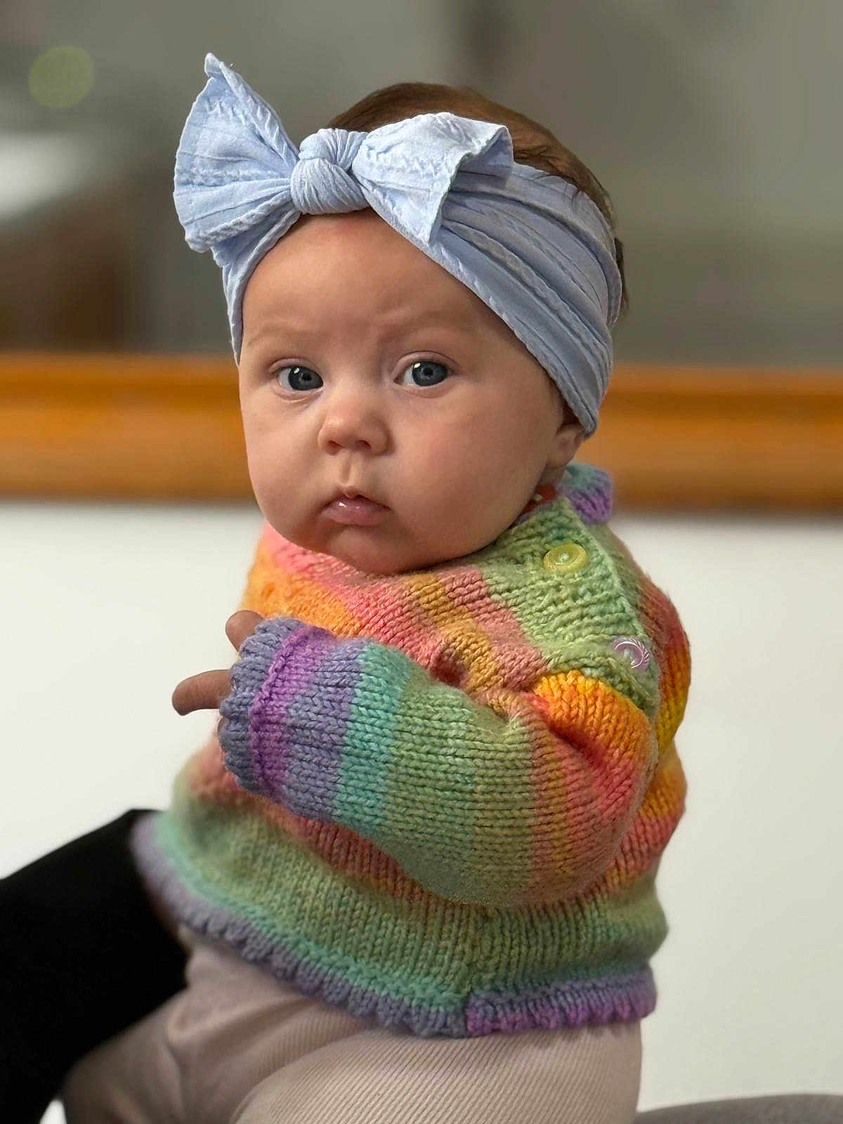 Phoebe is registered to the contest to win money with this photo: baby, child, headband, bow, knitted_sweater, rainbow_colors, cute, portrait, indoor, soft_light, face, chubby_cheeks, expression, person, clothing, infant, warm, colorful, sitting, closeup