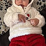 Lesly Bolivar is registered to the contest to win money with this photo: baby, child, hoodie, red_pants, fluffy_clothing, cute, face, infant, bed, patterned_bedspread, hand, eyes, indoor, soft_texture, warm_clothing, person, portrait, lying_down, young_child, cozy