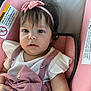 baby, child, infant, car_seat, pink, headband, bow, white_shirt, ruffled_sleeves, floral_pattern, clothing, seatbelt, cute, face, portrait, indoor, person, young_child, sitting, expression