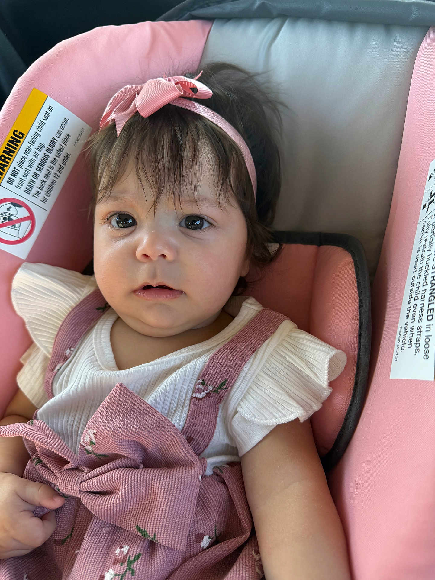 Lesly Bolivar is registered to the contest to win money with this photo: baby, child, infant, car_seat, pink, headband, bow, white_shirt, ruffled_sleeves, floral_pattern, clothing, seatbelt, cute, face, portrait, indoor, person, young_child, sitting, expression