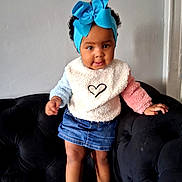 Angely joined the competition — help win amazing prizes! black_sofa, blue_bow, child, colorful_clothing, curly_hair, cute, denim_skirt, fashion, headband, heart_design, home, indoor, person, playful, standing, sweater, toddler, wall, white_shoes, young_child