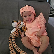 Alma participe au concours pour gagner de l'argent avec cette photo : baby, infant, smiling, peach_outfit, headband, plush_toy, tiger, stuffed_animal, couch, gray_furniture, happy, cute, child, indoors, portrait, sitting, legs, feet, hand, face