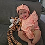 baby, infant, smiling, peach_outfit, headband, plush_toy, tiger, stuffed_animal, couch, gray_furniture, happy, cute, child, indoors, portrait, sitting, legs, feet, hand, face
