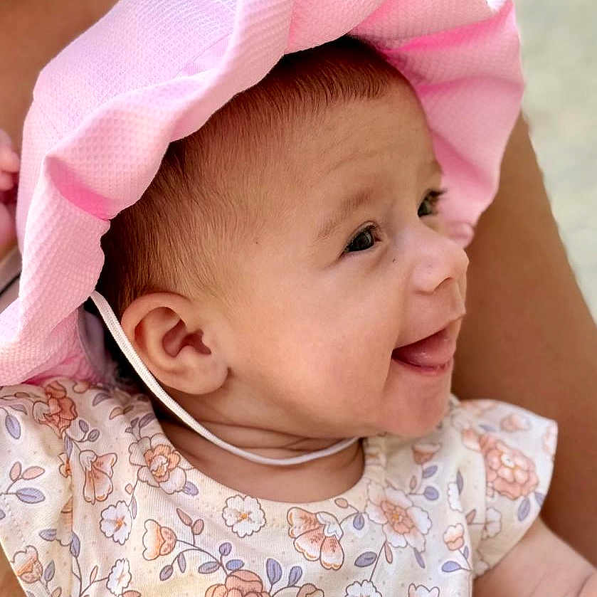 Alma a rejoint le concours — aidez-le/la à gagner de superbes lots ! arm, baby, child, clothing, cute, face, floral_dress, happy, hat, head, holding, infant, outdoor, parent, person, pink_hat, portrait, skin, smiling, summer