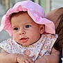 baby, child, pink_hat, floral_dress, cute, infant, face, eyes, arms, skin, person, holding, outdoor, daylight, portrait, expression, hand, headwear, curious, closeup