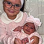 child, baby, sibling, pink_clothing, matching_outfits, headband, bow, glasses, smile, holding, couch, indoor, portrait, cute, family, happy, toddler, newborn, hands, cozy