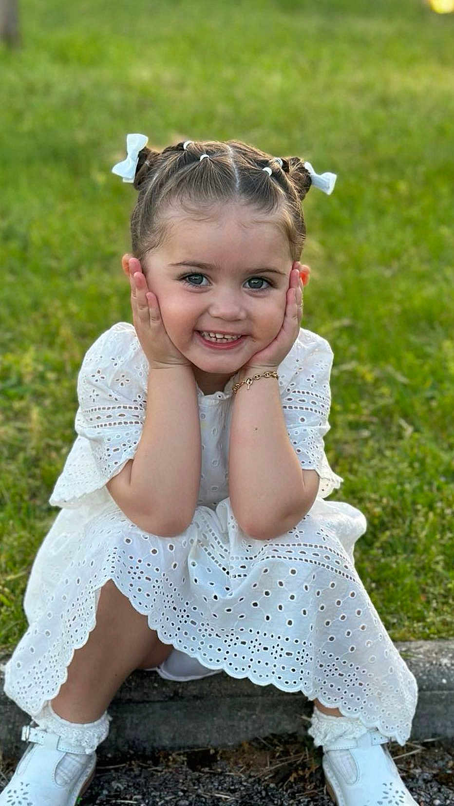 Hayden a rejoint le concours — aidez-le/la à gagner de superbes lots ! child, girl, white_dress, smiling, grass, outdoor, hair_bows, sitting, cute, portrait, happy, bracelet, shoes, sunlight, candid, fashion, young, playful, nature, daylight