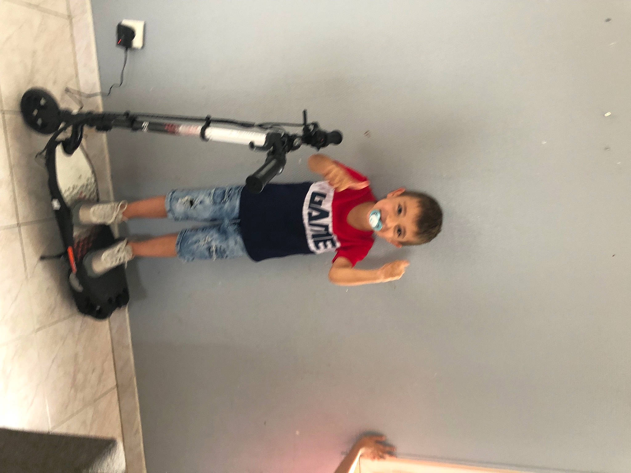 Tiago participe au concours pour gagner de l'argent avec cette photo : ceiling, elbow, electrical_wiring, flooring, fun, helmet, joy, machine, person, plaster, recreation, room, shelf, sports_equipment, t_shirt, thigh, tire, toddler, toy