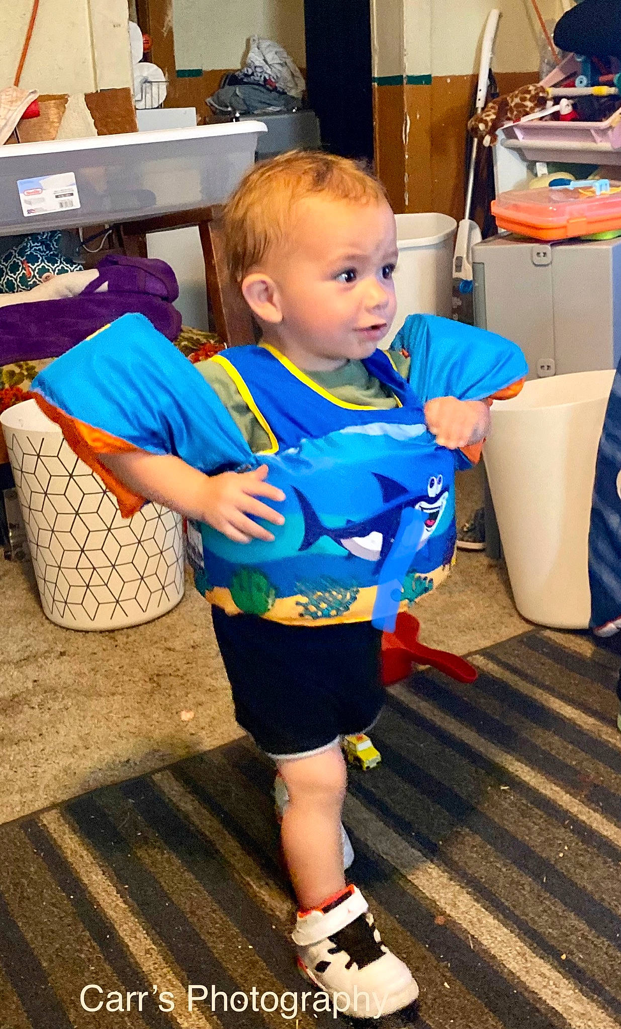 Korbyn is registered to the contest to win money with this photo: baby, box, chair, child, electric_blue, event, flooring, fun, head, human_leg, knee, leisure, person, room, shipping_box, shoe, shopping, shorts, t_shirt, thigh