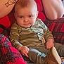 Kaiden is registered to the contest to win money with this photo: baby, child, infant, person, striped_clothing, green_outfit, booties, quilt, plaid, tattoo, arm, face, expression, sitting, indoors, cozy, cute, cheeks, hands, relaxing
