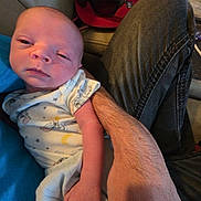 Ezekiel is registered to the contest to win money with this photo: baby, newborn, infant, onesie, sleepy, arm, hand, denim, jeans, cap, red_cap, face, person, indoor, couch, blanket, casual, home, resting, holding
