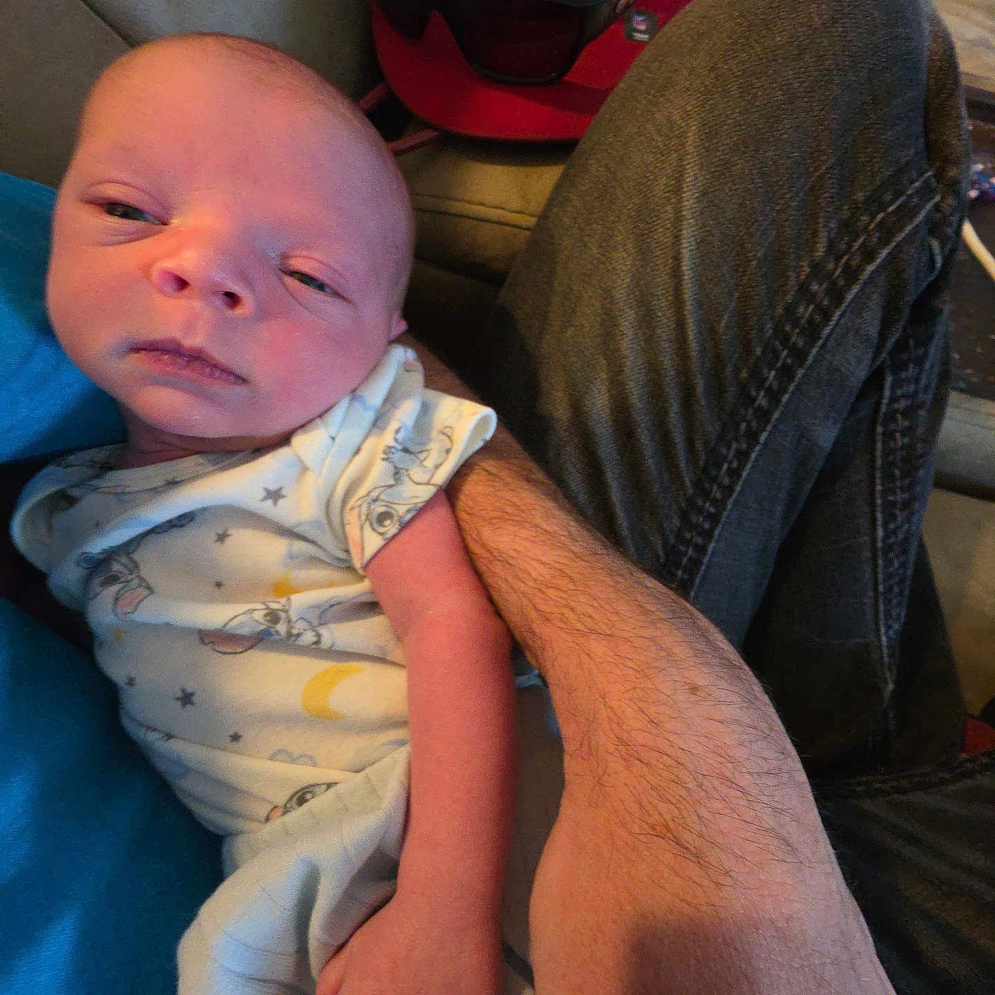 Ezekiel is registered to the contest to win money with this photo: baby, newborn, infant, onesie, sleepy, arm, hand, denim, jeans, cap, red_cap, face, person, indoor, couch, blanket, casual, home, resting, holding