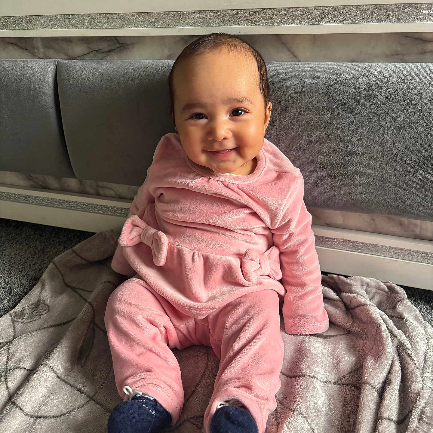 Amreen is registered to the contest to win money with this photo: apparel, baby, blanket, carpet, child, cozy, cute, face, floor, happy, headboard, indoors, infant, pink_clothing, portrait, sitting, smiling, soft_texture, warm_lighting, young_child