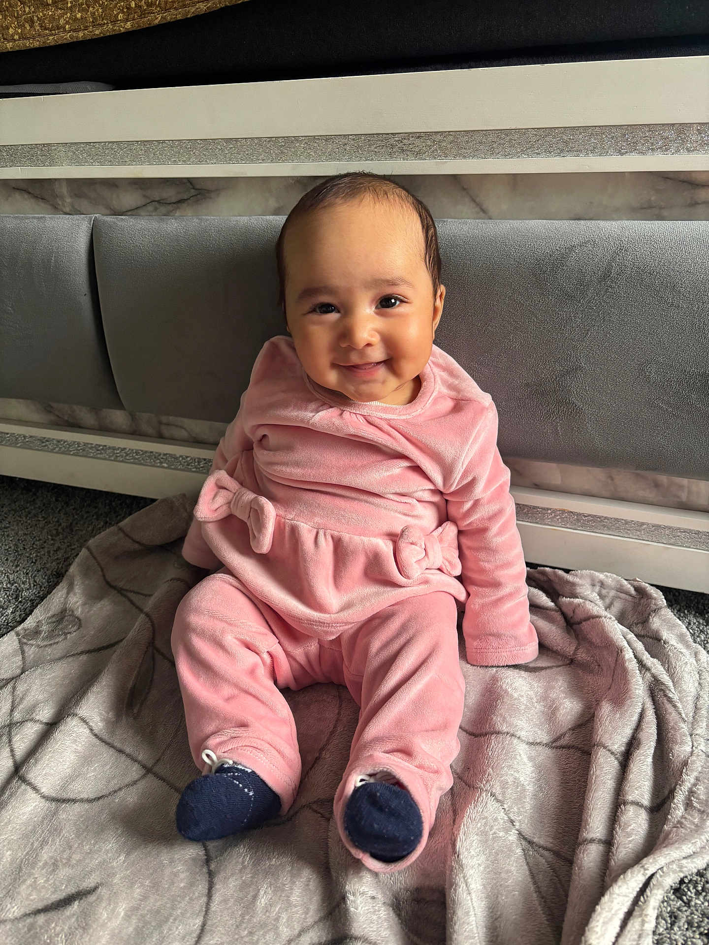 Amreen is registered to the contest to win money with this photo: baby, infant, smiling, pink_clothing, blanket, sitting, indoors, face, cute, child, headboard, carpet, happy, cozy, portrait, apparel, young_child, soft_texture, warm_lighting, floor