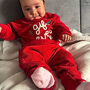Amreen joined the competition — help win amazing prizes! baby, blanket, child, comfort, cozy, cute, face, hand, head, indoors, infant, pants, pink_socks, portrait, red_clothing, seated, smiling, soft_fabric, sweater, warm