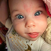 Eleanor is registered to the contest to win money with this photo: baby, close_up, blue_eyes, face, expression, white_shirt, golden_text, blanket, hand, red_nail_polish, cozy, indoors, child, cute, portrait, skin, person, infant, young_child, sleepwear