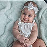 baby, infant, headband, bow, white_clothing, smile, face, blue_eyes, skin, soft_blanket, texture, cute, portrait, child, sitting, hands, happy, adorable, young, indoor