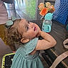 toddler, child, curly_hair, bow, dress, table, sippy_cup, flowers, roses, vase, indoor, person, adult, reflection, glass_wall, greenery, chair, smiling, happy, casual_clothing