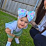 toddler, child, grass, outdoor, fence, bow, headwear, smile, white_shoes, green_shorts, white_shirt, person, adult, crouching, bracelet, earrings, long_hair, daylight, casual_clothing, happy