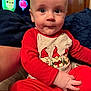 baby, child, infant, red_clothing, pajamas, gnomes, holiday_theme, indoor, person, face, hand, expression, couch, blanket, background, television, cartoon, colorful, cute, seated