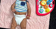 Alex is registered to the contest to win money with this photo: baby, infant, diaper, striped_shirt, toy, colorful_toy, gears, pink_mat, quilted_mat, black_rug, barefoot, foot, smiling, lying_down, indoors, child, cute, playtime, person, happy