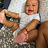 baby, smiling, infant, foot, hand, quilt, blanket, lying_down, happy, cute, child, person, skin, casual_clothing, indoor, playful, red_bracelet, patterned_textile, closeup, portrait