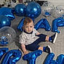 balloons, birthday, blue_balloons, carpet, celebration, child, clothing, curious, face, footwear, home, indoor, letters, party, person, shirt, shorts, sitting, toddler, transparent_balloons