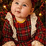 baby, child, christmas, cozy, cute, festive, greenery, hands, headband, holiday, indoor, lace, lights, plaid_dress, portrait, red_bow, sitting, smiling, warm_lighting, young_child