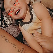 George is registered to the contest to win money with this photo: arm, blanket, child, closeup, curly_hair, digital_sticker, fabric, face, happy, indoor, kiss_marks, laughing, person, playful, skin, sleeveless_shirt, smiling, tattoo, tattooed_arm, toddler