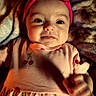 baby, child, infant, pink_headband, bow, cherry_pattern, dress, blanket, portrait, smile, face, cute, indoors, soft_lighting, cozy, hand, young_child, apparel, person, closeup