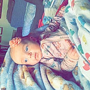 Saylor is registered to the contest to win money with this photo: baby, blanket, flower_headband, indoor, infant, person, portrait, cozy, soft_texture, furniture, table, bottle, household_items, curious, child, clothing, patterned_blanket, resting, cute, head