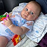 Emiliano is registered to the contest to win money with this photo: baby, child, infant, portrait, face, blue_eyes, wide_eyed, lying_down, sitting, rattle, toy, lion_toy, blanket, cushion, onesie, clothing, indoor, car_seat, smiling, close_up
