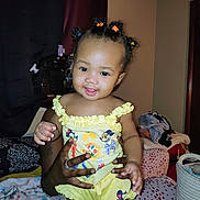 Eerie is registered to the contest to win money with this photo: toddler, child, smiling, yellow_outfit, hair_ties, indoor, bedroom, blanket, clothing, hands, person, furniture, basket, curtains, wall, door, happy, portrait, baby, room