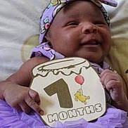Naomi is registered to the contest to win money with this photo: baby, infant, smiling, purple_outfit, headband, sign, celebration, milestone, month_marker, cute, happy, child, portrait, indoors, cushion, hand, face, person, tutu, soft