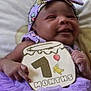 baby, infant, smiling, purple_outfit, headband, sign, celebration, milestone, month_marker, cute, happy, child, portrait, indoors, cushion, hand, face, person, tutu, soft