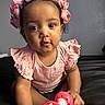 baby, child, infant, pink_bow, pink_clothing, toy, indoor, portrait, cute, curly_hair, sitting, face, skin, hands, eyes, expression, headband, playful, closeup, person