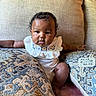 arm, baby, child, chubby_cheeks, couch, curly_hair, cute, embroidery, face, foot, furniture, hand, indoors, infant, patterned_pillow, pillow, portrait, sitting, skin, white_outfit