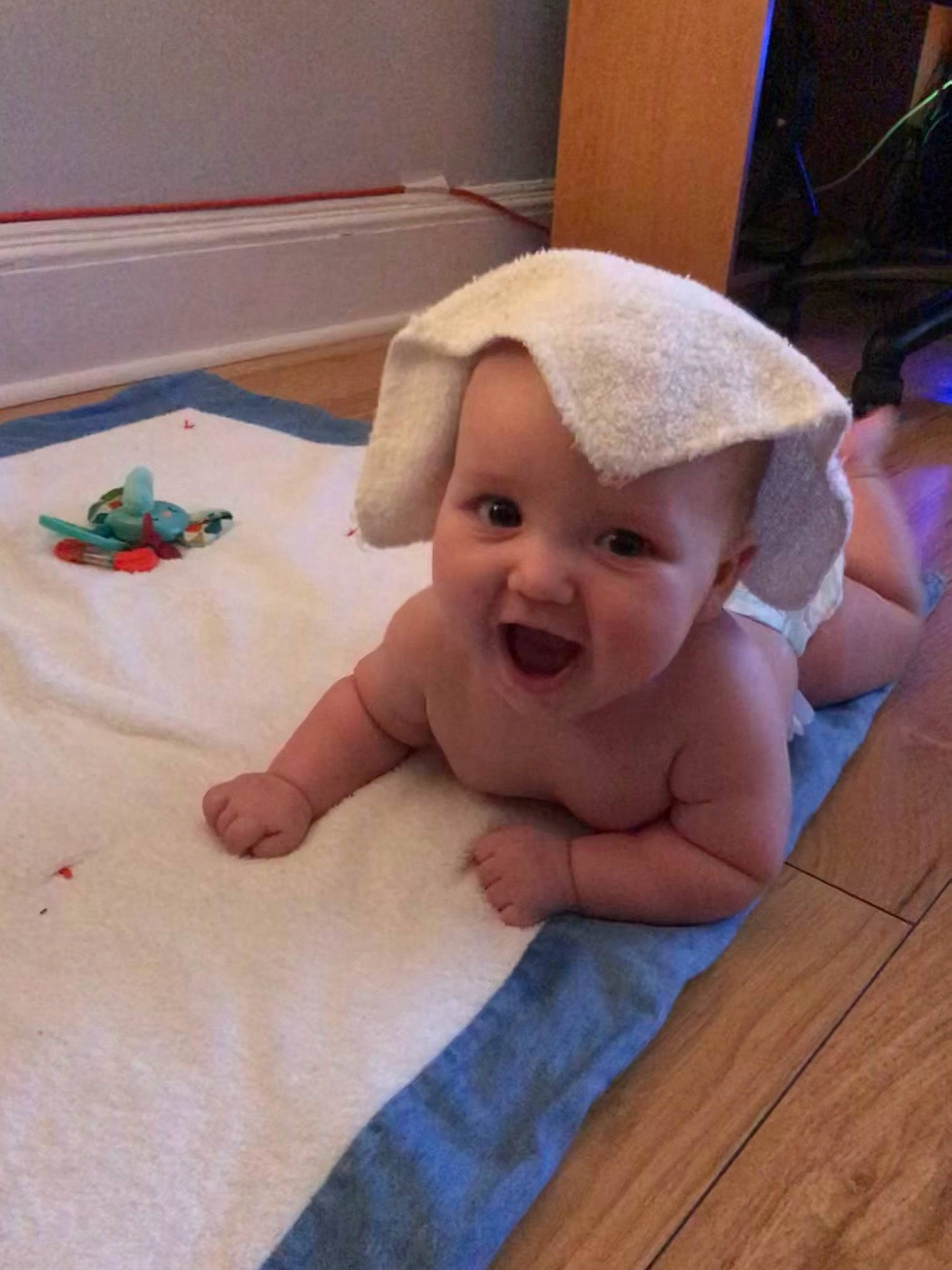 James participe au concours pour gagner de l'argent avec cette photo : baby, baby_laughing, baby_toddler_clothing, cap, child, comfort, fashion_accessory, floor, flooring, fun, happy, hardwood, headgear, linens, person, sitting, skin, smile, thumb, toddler