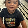 toddler, child, smiling, curly_hair, black_tshirt, diaper, sitting, rug, indoor, happy, cute, face, person, baby, young_child, portrait, expression, clothing, floor, home